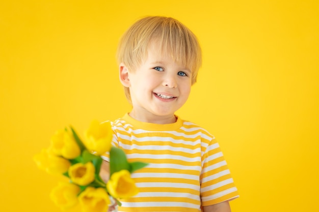 Criança feliz segurando buquê de tulipas primavera contra parede amarela.