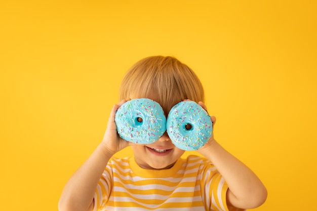 Criança feliz segurando um donut com cobertura contra a parede amarela