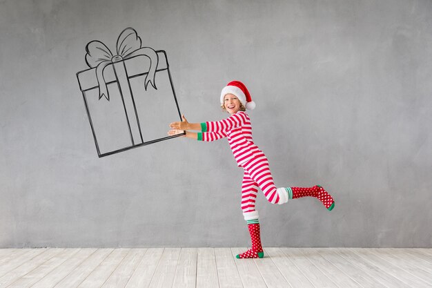 Criança feliz segurando uma caixa de presente de Natal. Garoto engraçado brincando em casa