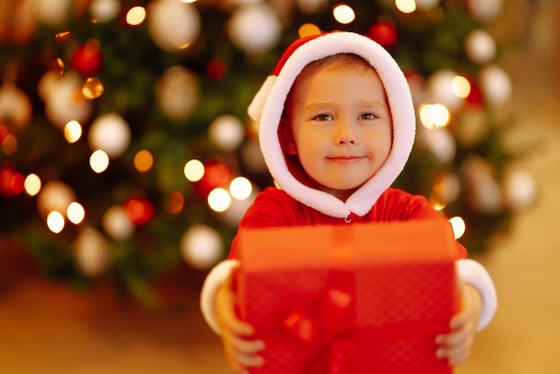 Criança feliz segurando uma caixa de presente vermelha nas luzes de fundo.