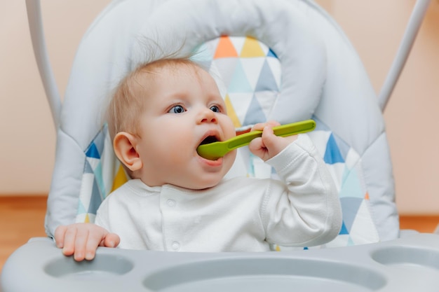 Criança feliz segurando uma colher em uma cadeira alta comida para bebê