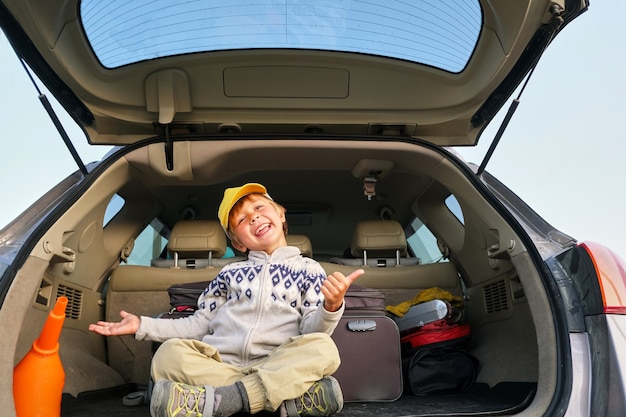 Criança feliz sentada no porta-malas do carro para a viagem