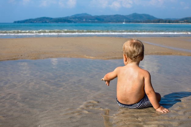 Criança feliz sentado na água à beira-mar no verão vista traseira