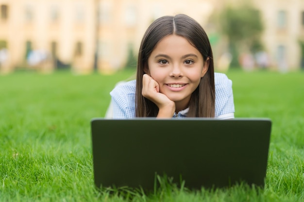 Criança feliz trabalhando no laptop. Educação online. de volta à escola. menina adolescente usa computador na grama verde no parque. criança com notebook. nova tecnologia na vida moderna. estudar. Comprar online.