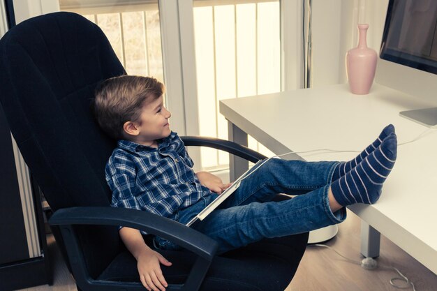 Foto criança feliz usando computador e vendo algo na internet enquanto se relaxa em casa