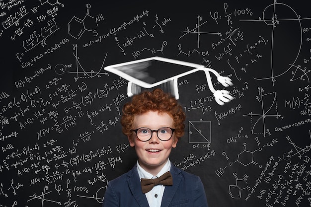Criança feliz usando óculos de chapéu de formatura e uniforme de estudante com formação científica
