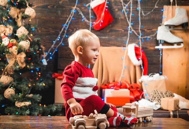 Criança feliz vestida com roupas de inverno perto da árvore de natal, noite de inverno em casa