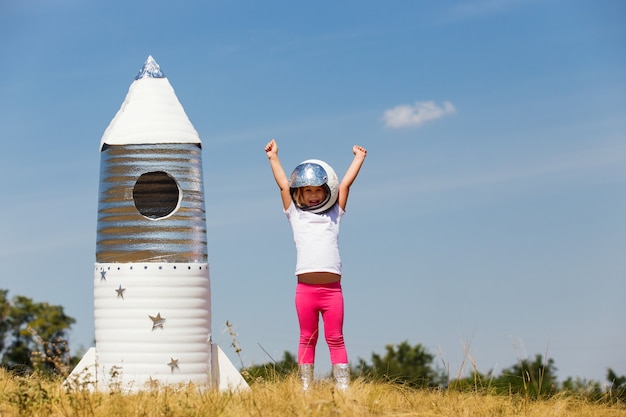 Criança feliz vestida com uma fantasia de astronauta, brincando com um foguete feito à mão.