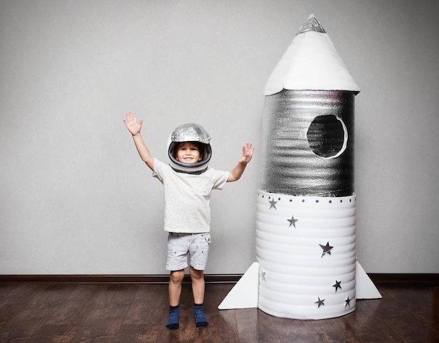 Criança feliz vestida com uma fantasia de astronauta, brincando com um foguete feito à mão.