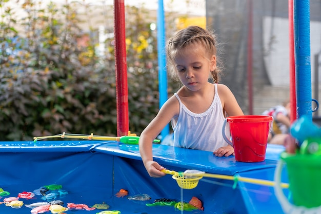 Criança fisher pegando peixe de brinquedo de plástico na piscina parque de diversões dia de verão menina se divertindo na pesca festival de carnaval de entretenimento para crianças