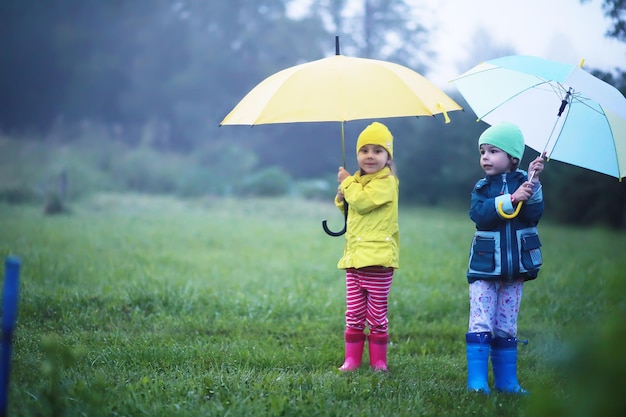 Criança fofa brincando na chuva com guarda-chuva em um dia nublado de outono em uma estrada rural