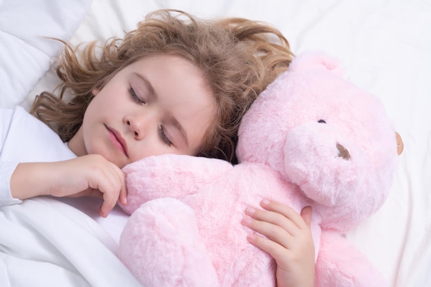 Criança fofa do sono diário dorme com um ursinho de pelúcia na cama criança dormindo