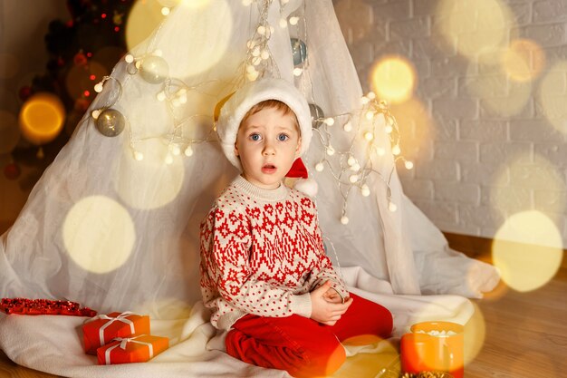 Criança fofa e alegre brincar perto da árvore de natal, é um milagre