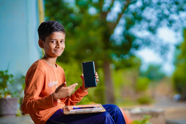 Criança indiana estudando em casa e mostrando a tela do smartphone.