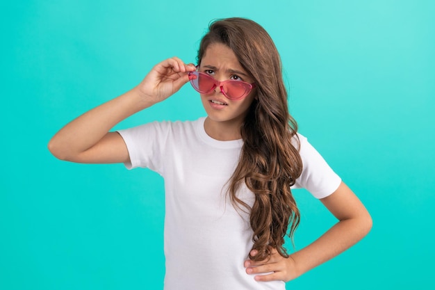 Criança infeliz, cabelo longo e encaracolado em óculos de sol estilo casual no estilo de moda de fundo azul