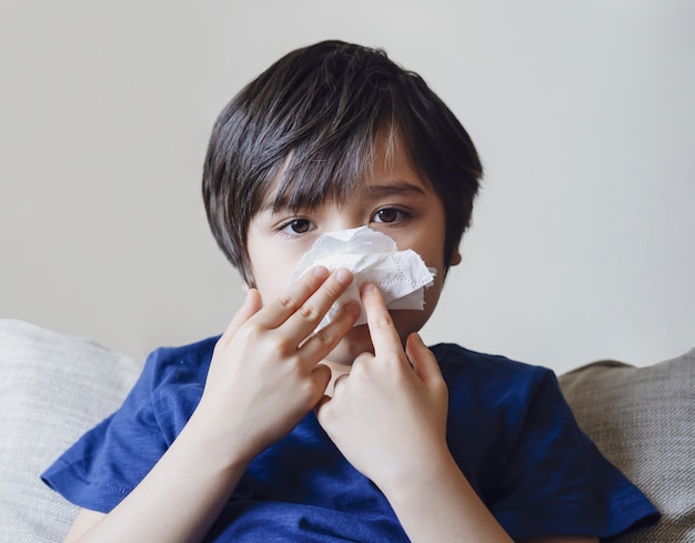 Criança insalubre soprando nariz em tecido, Criança que sofre de coriza ou espirros, Um garoto pega um resfriado quando a estação muda, infância limpando o nariz com tecido