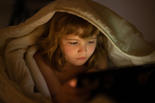 Criança jogando jogo no tablet na cama à noite crianças com mídia social criança deitada na cama jogando um