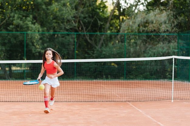 Criança jogando tênis na quadra ao ar livre. menina com raquete de tênis e bola no clube de esporte. exercício ativo para crianças