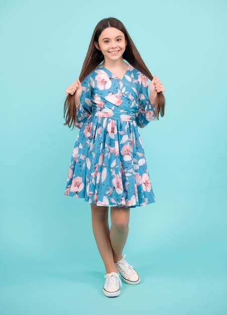 Criança jovem adolescente graciosa em vestido isolado em fundo azul Adolescente bonita em roupas de verão Adolescente feliz emoções positivas e sorridentes