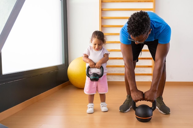 Criança levantando kettlebell com o pai