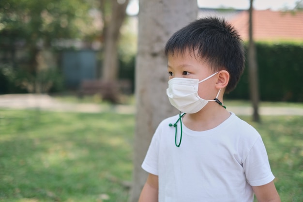 Criança linda asiática de 5 anos usando máscara protetora médica na natureza no parque, conceito de coronavírus, novo estilo de vida normal e conceito de poluição do ar pm 2.5, foco suave e seletivo