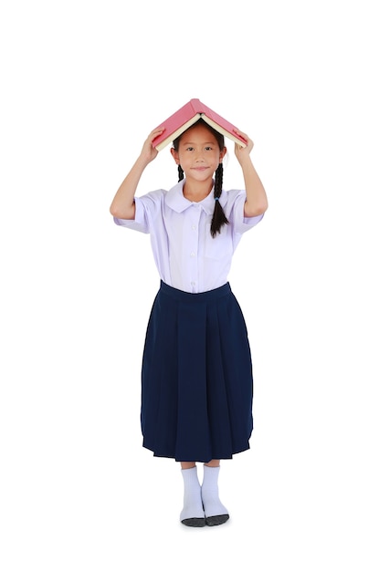 Criança menina asiática em uniforme escolar tailandês em pé com segurar a capa do livro aberta sobre a cabeça isolada no fundo branco. Comprimento total com traçado de recorte