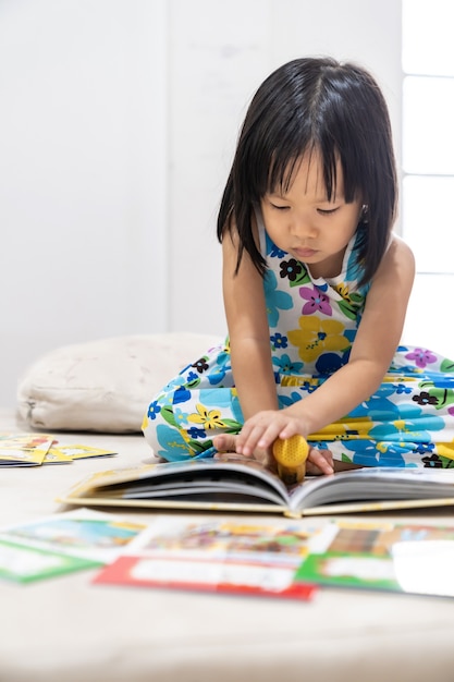 Criança menina asiática lendo livro interativo na sala de estar em casa como ensino doméstico