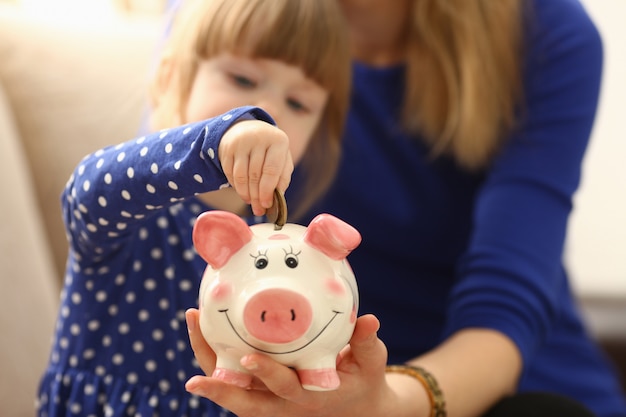 Criança menina braço colocando moedas no piggybank