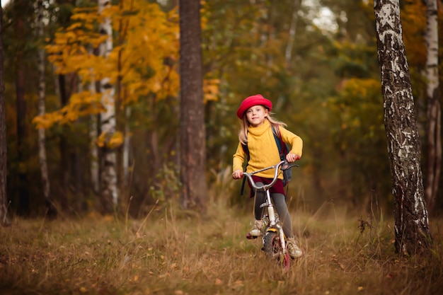 criança, menina em uma bicicleta em roupas brilhantes e um chapéu, no parque no outono