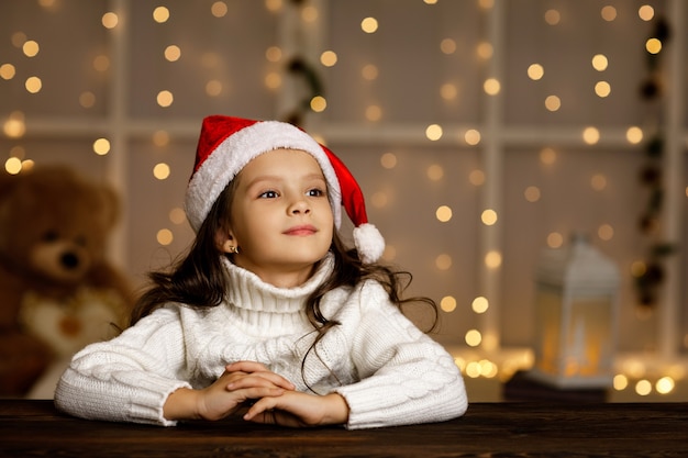 Criança menina feliz com chapéu de Papai Noel escrevendo uma lista de desejos ou uma carta para o Papai Noel