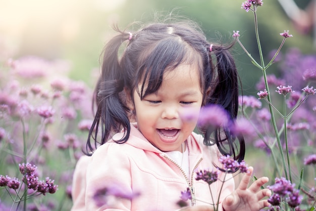 Criança, menina feliz, correndo e se divertindo no campo de flores roxas