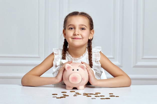Criança menina feliz economizando dinheiro para o futuro no cofrinho rosa