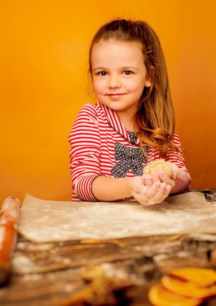 criança, menina prepara a massa para biscoitos em um fundo de madeira