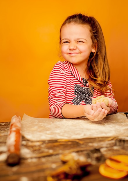 criança, menina prepara a massa para biscoitos em um fundo de madeira