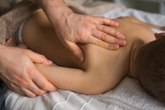 Criança menino relaxa de uma massagem terapêutica. Fisioterapeuta, trabalhando com o paciente na clínica, nas costas de uma criança