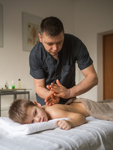 Criança menino relaxa de uma massagem terapêutica. fisioterapeuta, trabalhando com o paciente na clínica, nas costas de uma criança