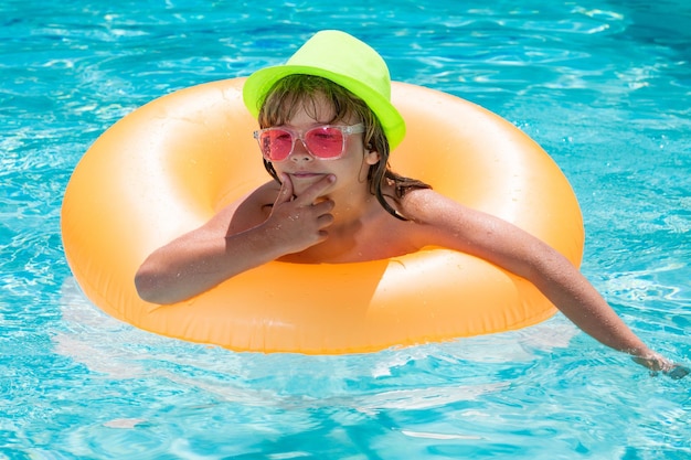 Criança menino relaxando na piscina Criança nadando na piscina de água Menino na piscina no anel inflável Criança nadando com boia laranja