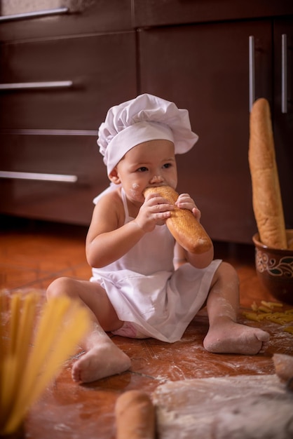 criança morde um pão em uma fantasia de cozinheiro