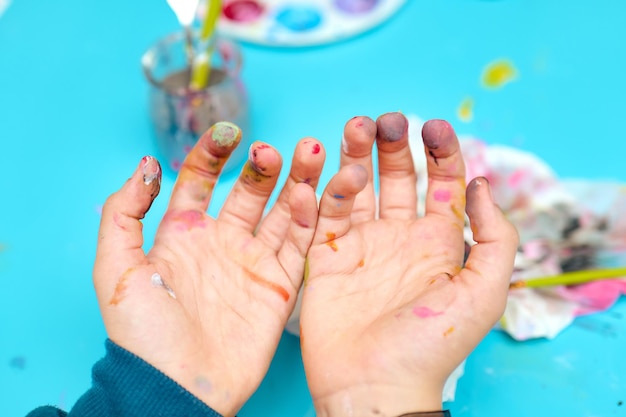 Criança mostrando as mãos sujas depois de pintar com aquarelas sem rostos são mostrados