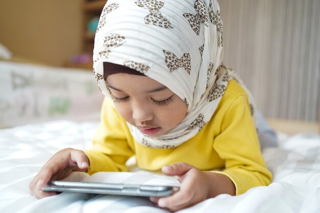 Criança muçulmana asiática jogando smartphone em casa.