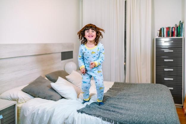 Criança muito feliz pulando na cama de pijama antes de ir para a cama