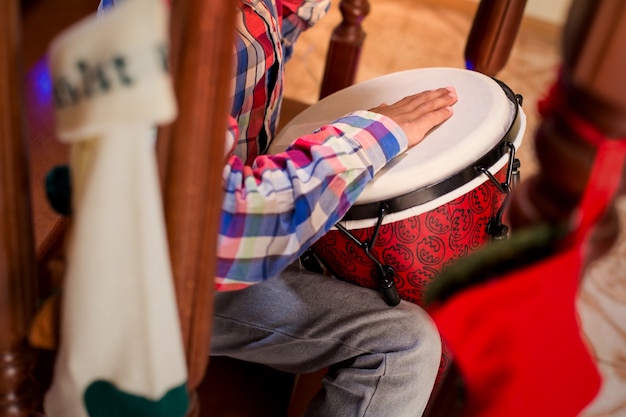 Criança mulata tocando tambor de percussão menino toca djembe nas escadas animada música de natal em casa litt ...