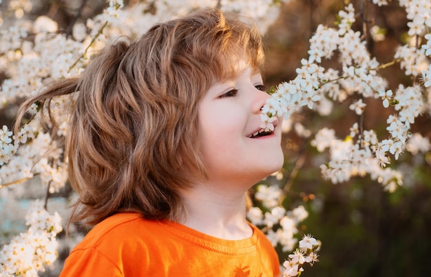 Criança na árvore florescendo no parque primavera Menino sorridente ao ar livre Jardim florido