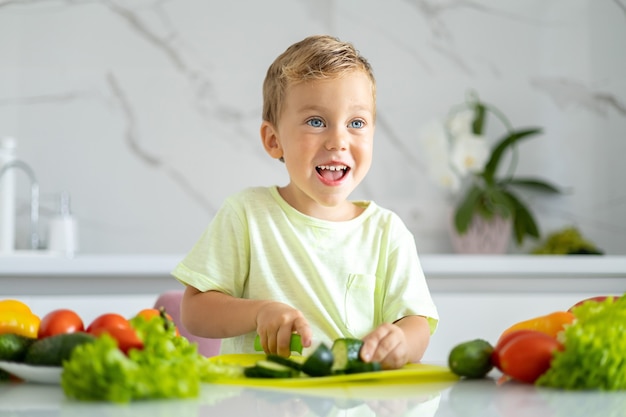 criança na cozinha cortando vegetais para salada bebê sorrindo conceito de alimentação saudável vegetariano