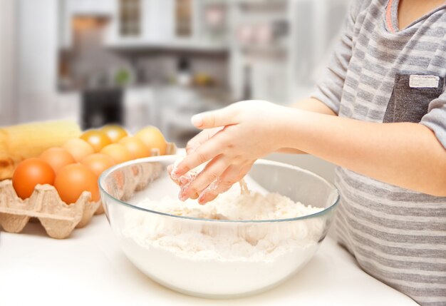 Criança na cozinha de casa preparando massa para pizza ou outro alimento.