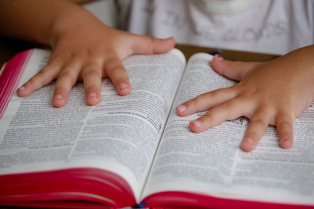 Criança na mesa lendo a Bíblia Sagrada e folheando-a