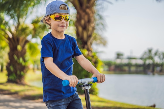 Criança na scooter no parque crianças aprendem a andar de skate garotinho patinando no dia ensolarado de verão atividade ao ar livre para crianças na rua residencial segura esporte ativo para criança pré-escolar