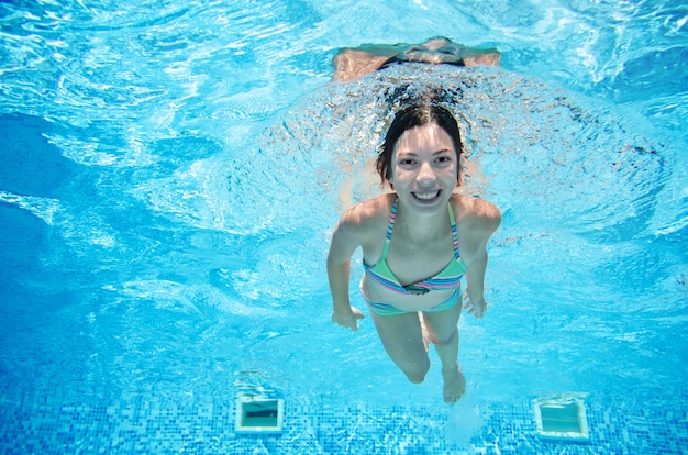 Criança nada debaixo d'água na piscina, garota adolescente ativo feliz mergulha e se diverte sob a água, fitness criança e esporte em férias em família no resort