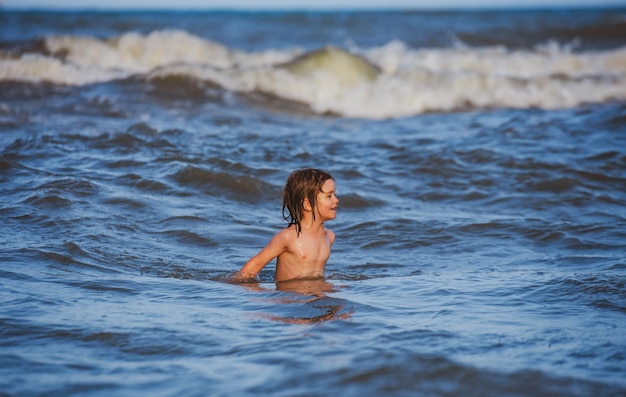 Criança nadando, se divertindo e pulando nas ondas do mar, férias para a família