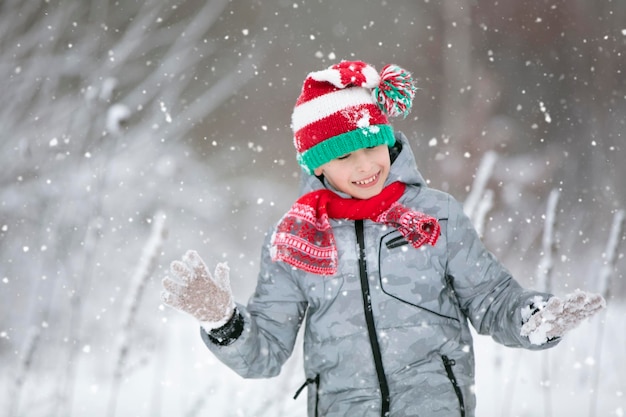 Criança no inverno na floresta Um garotinho, uma criança com roupas de inverno andando sob a neve